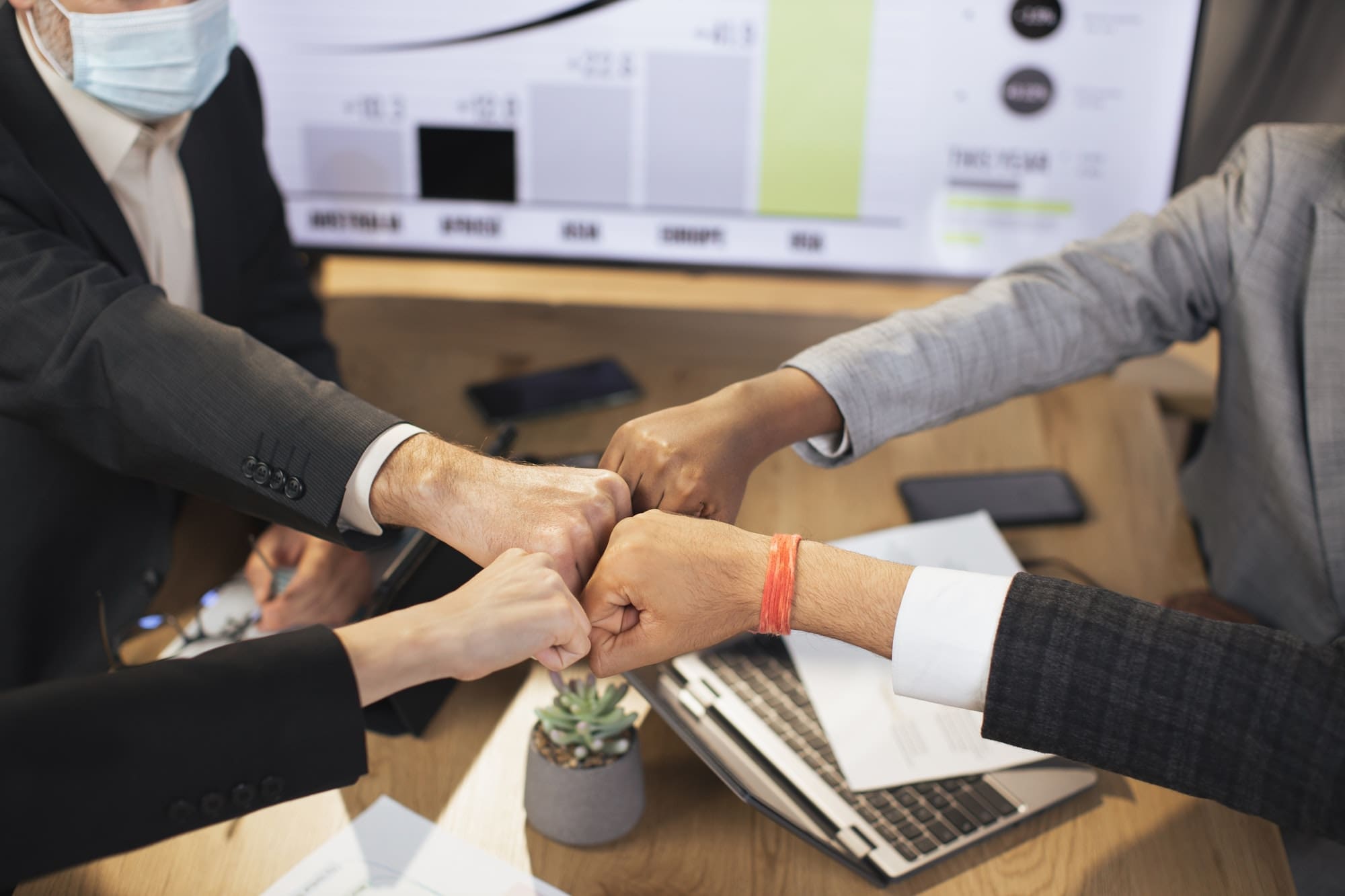 Close up of different ethnicity business people, putting fists together over workplace